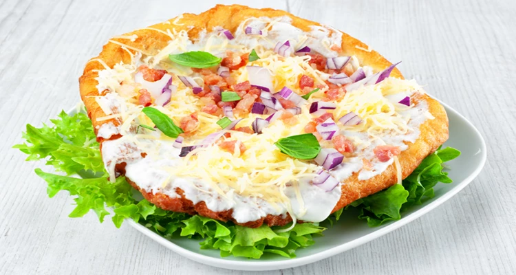 Lángos mit Sauerrahm, Speck und Zwiebel auf Blattsalat